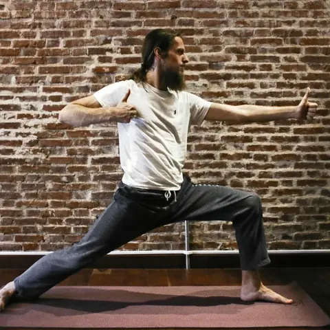 A male yogi performing archer pose in a yoga studio, a red brick wall in the background