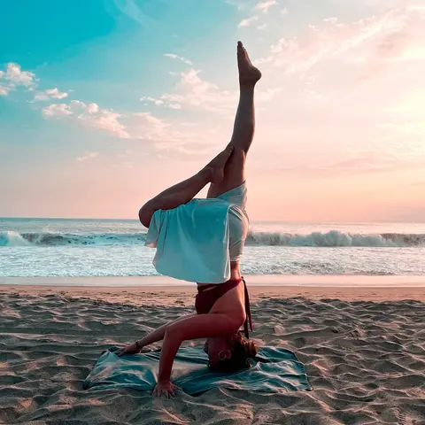 A female yogi performing an elegant vinyasa headstand pose on a beach during early sunset