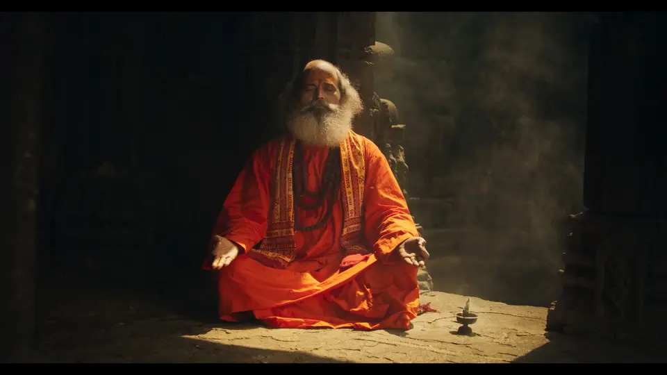 A monk in orange robes meditaing in a dark-lit temple