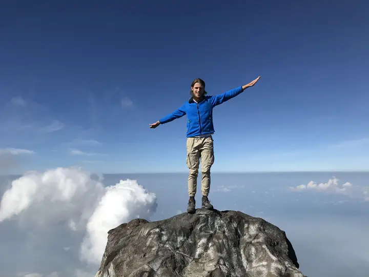 A man standing on a mountain peak, a clear blue sky in the background, a few clouds floating in the sky