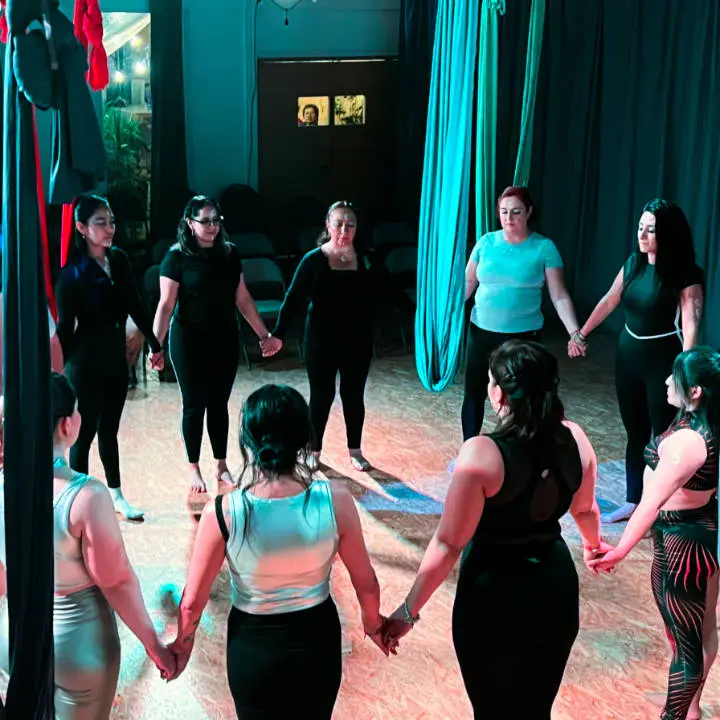 A group of teacher training students standing in a cricle and holding hands, eyes closed, meditating together