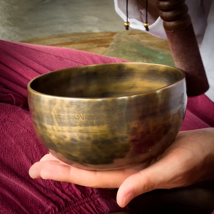 A close up on a yogi playing a tibetan sound bowl during a sound healing session