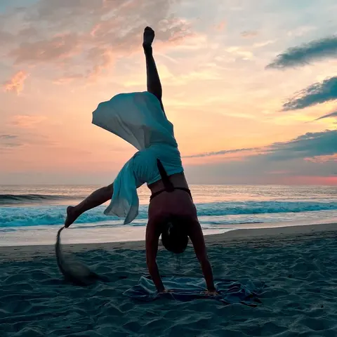 A female yogi entering a hand stand on a beach during sunset